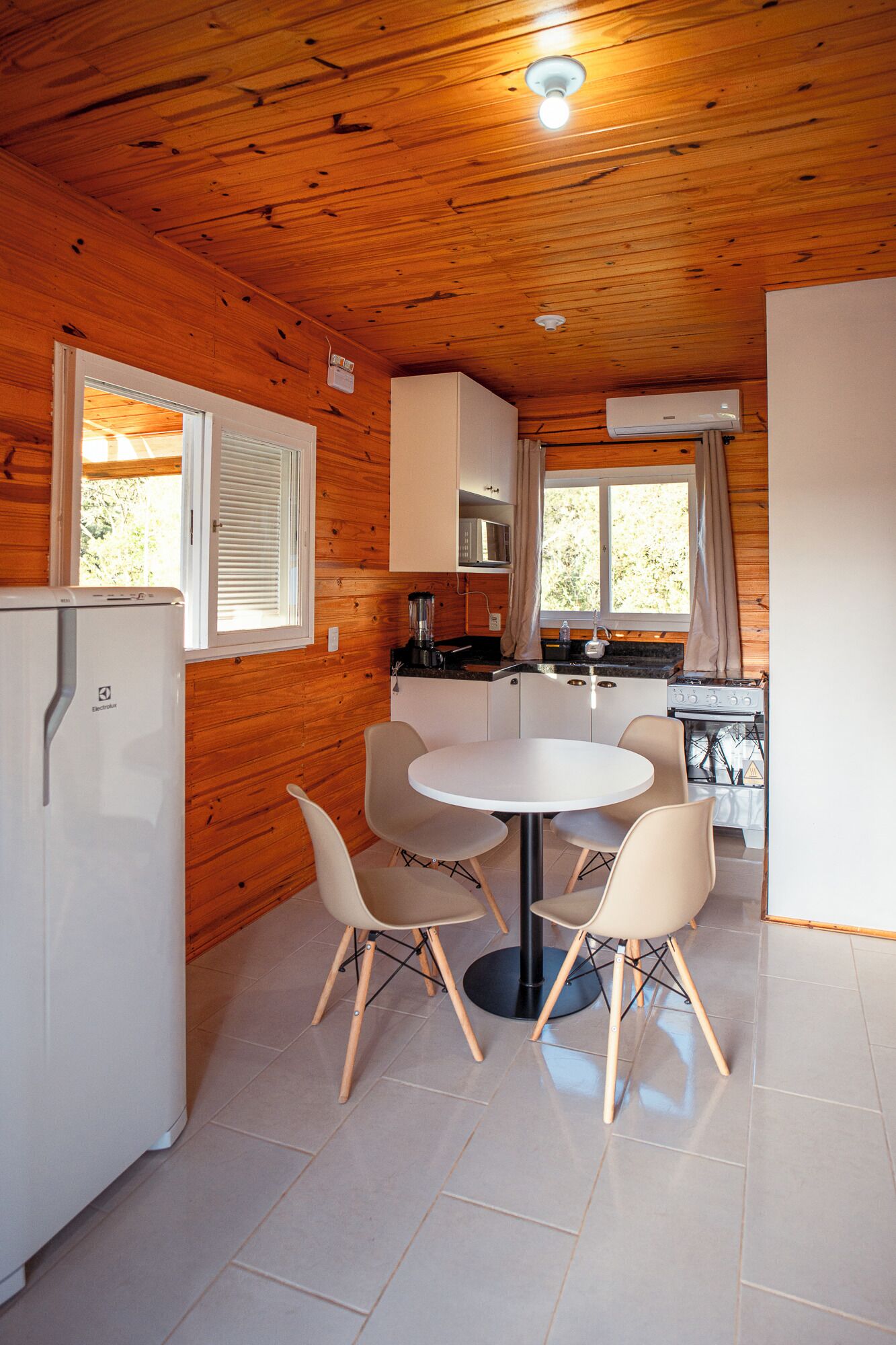 A compact kitchen with a round table and four chairs, a refrigerator, a stove, and a microwave.