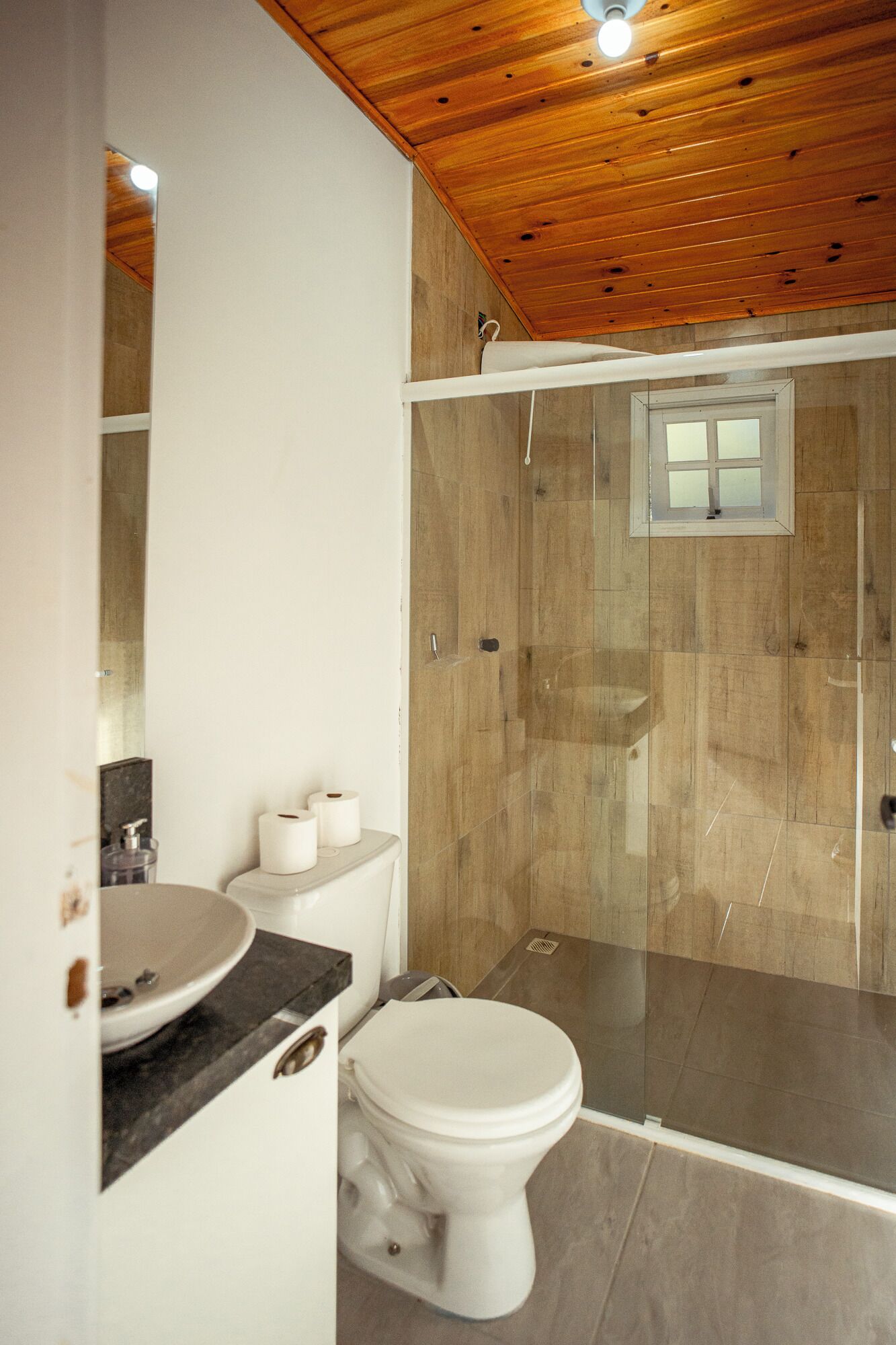 A bathroom with a wooden ceiling, a shower with a glass door, a toilet, and a sink with a marble countertop.