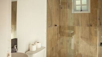 A bathroom with a wooden ceiling, a shower with a glass door, a toilet, and a sink with a marble countertop.