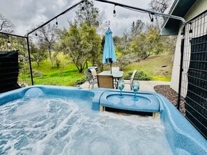 A hot tub with a table and chairs, surrounded by a fence and trees. - Lighthouse Suite - Dog Friendly Home - Hot Tub - BBQ - Full Kitchen - Sleeps 4 (Coarsegold)