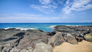 A rocky shoreline with waves crashing against the rocks and a clear blue sky above.