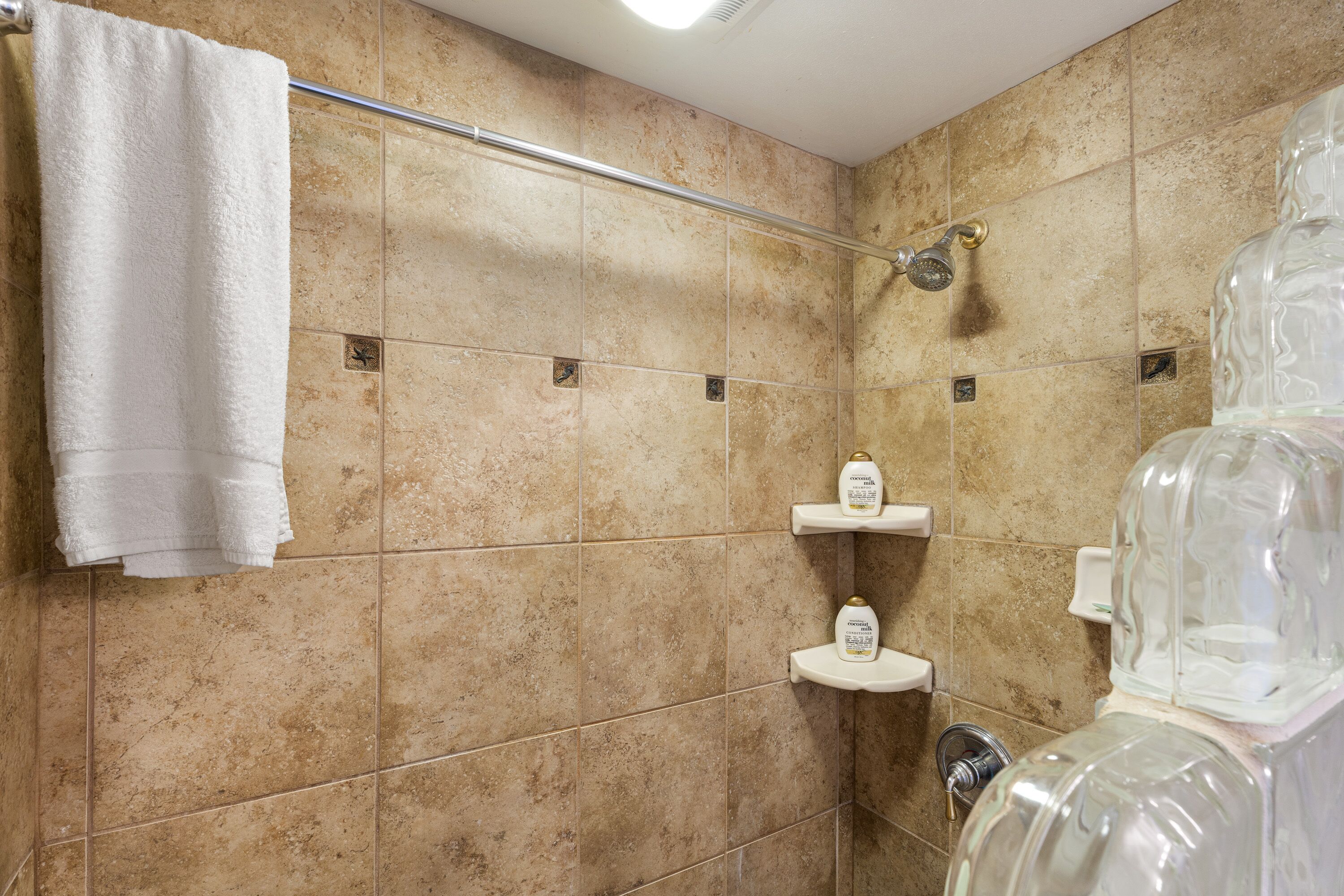 A bathroom with beige tiles, a white towel, and a glass shower enclosure.
