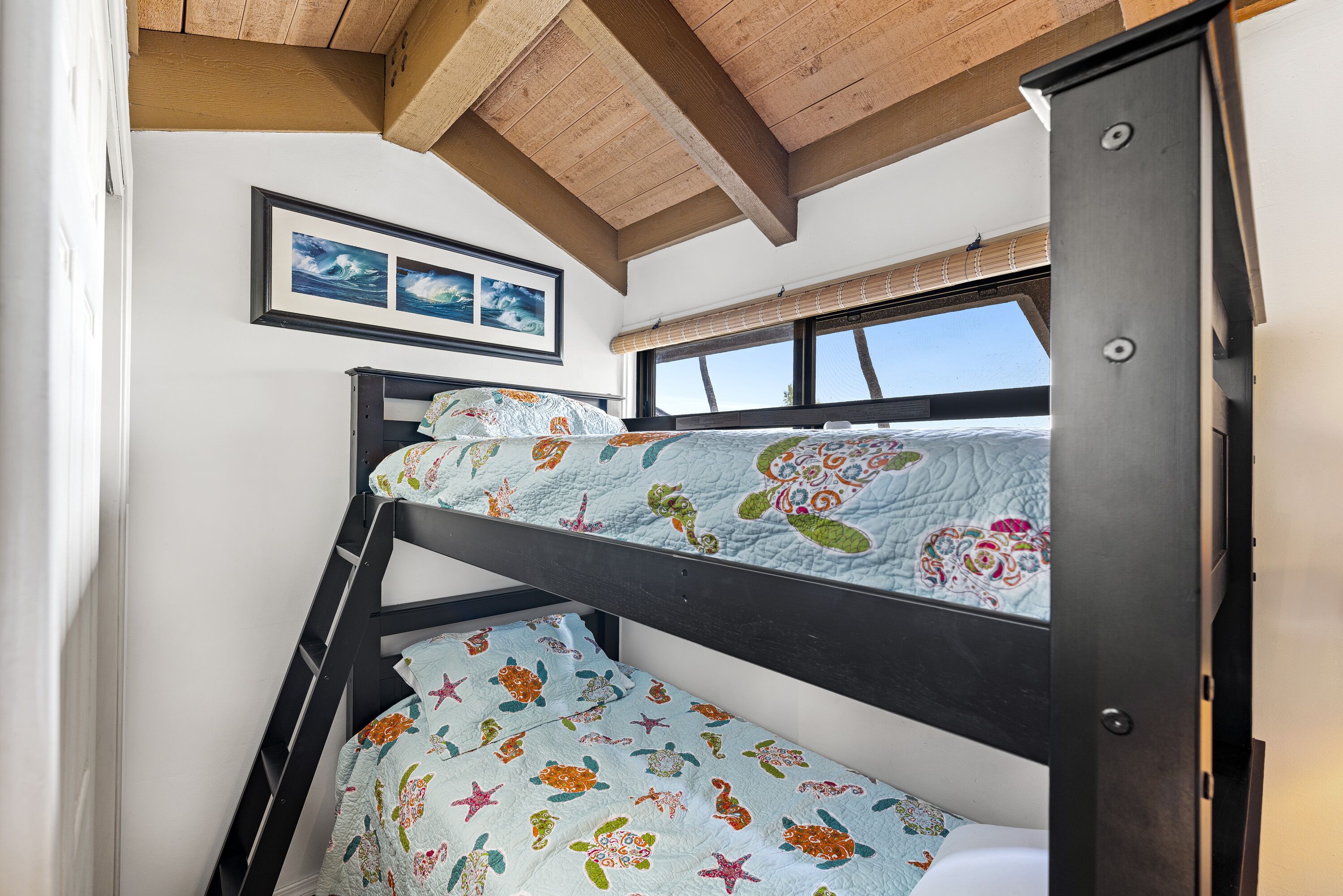 A bunk bed with a colorful quilt, wooden ceiling beams, and a window with a view.