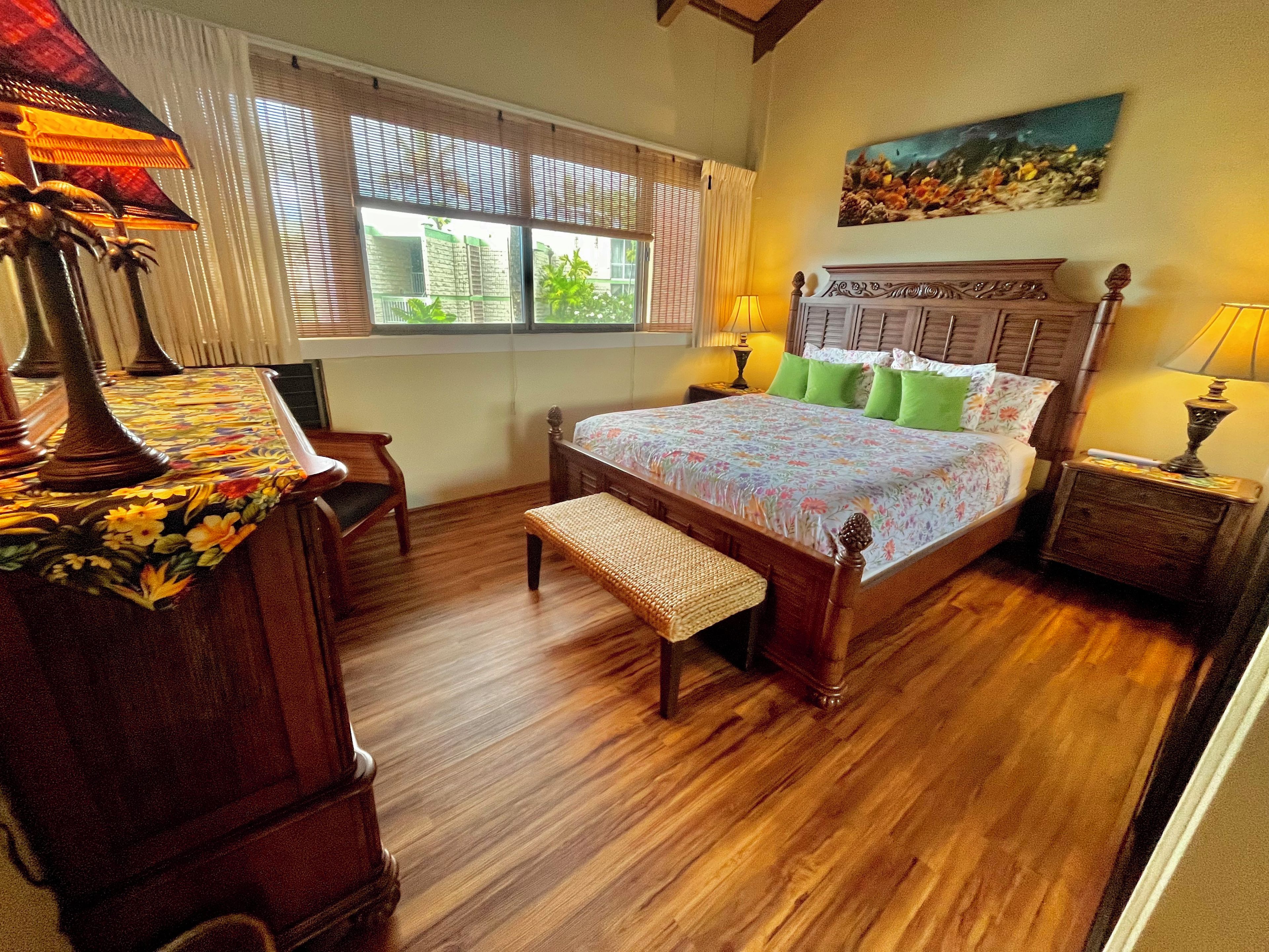 Quarto com cama de madeira, um banco, uma escrivaninha e janela com persianas.