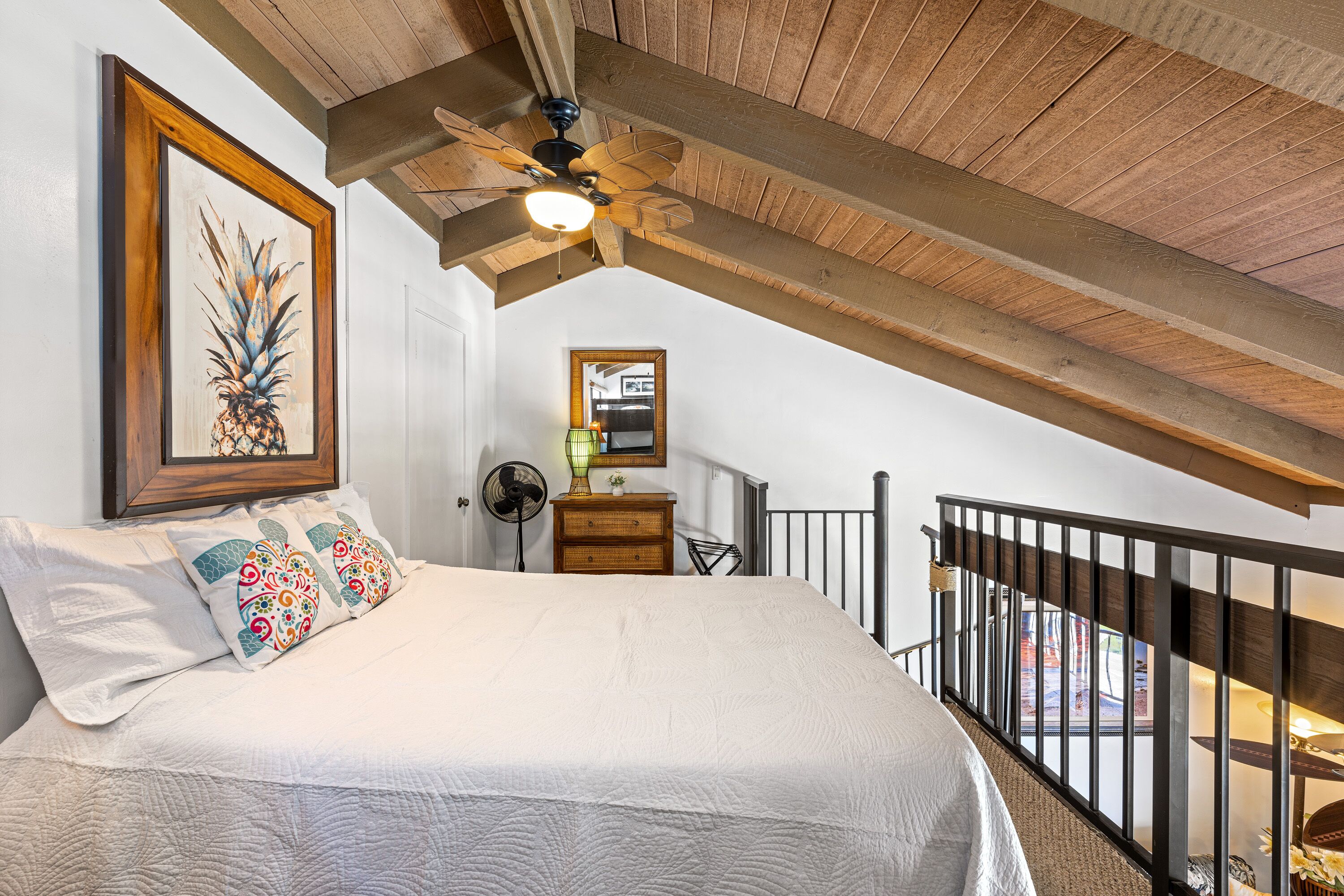 Une chambre à coucher avec un grand lit, un ventilateur de plafond, un plafond en bois, une commode et une rambarde de balcon.
