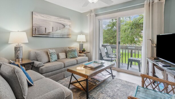 A living room with a sofa, coffee table, and TV, a ceiling fan, and a view of a deck and trees. -  One block to Beach! Clean, Bright, newly renovated 3BR 2BA Flat  (Fernandina Beach)