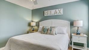 A bedroom with a bed, two bedside tables, a ceiling fan, and a wall-mounted artwork. -  One block to Beach! Clean, Bright, newly renovated 3BR 2BA Flat  (Fernandina Beach)