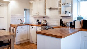 Une cuisine moderne avec des meubles blancs, un plan de travail en bois et divers appareils, notamment une machine à café et un grille-pain.