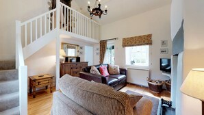 A spacious living room with a staircase, a fireplace, a television, and a large window. - Pant Glas - 1 Bedroom Cottage, in the countryside (Dwygyfylchi)