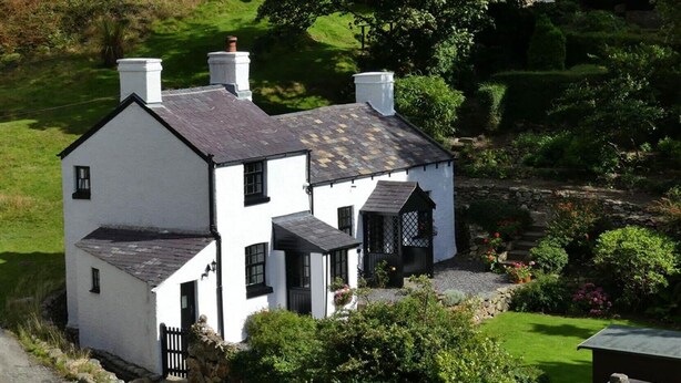A white two-story house with a sloped roof, multiple chimneys, and a stone wall surrounding the property. - Pant Glas - 1 Bedroom Cottage, in the countryside (Dwygyfylchi)