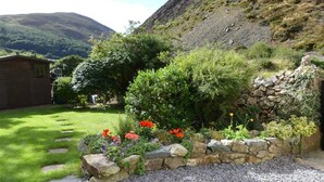 A garden with a stone wall, a wooden shed, and a grassy area with a mountain in the background. - Pant Glas - 1 Bedroom Cottage, in the countryside (Dwygyfylchi)