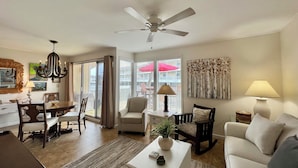 A living room with a ceiling fan, a dining area with a table and chairs, a sofa, and a coffee table with decorative items. - Relaxing 1BR Canal Retreat w/ Beach Access (Destin)