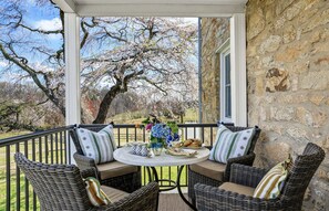 A covered outdoor seating area with wicker furniture, a table with a vase of flowers, and a stone wall. - Historic Farmhouse on Sprawling  55 acre Horse Farm (Washington)