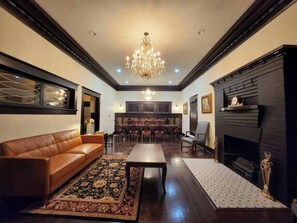 Un salón amplio con un sofá de cuero marrón, una mesa de centro, una araña, una chimenea y un comedor con muebles de madera.
