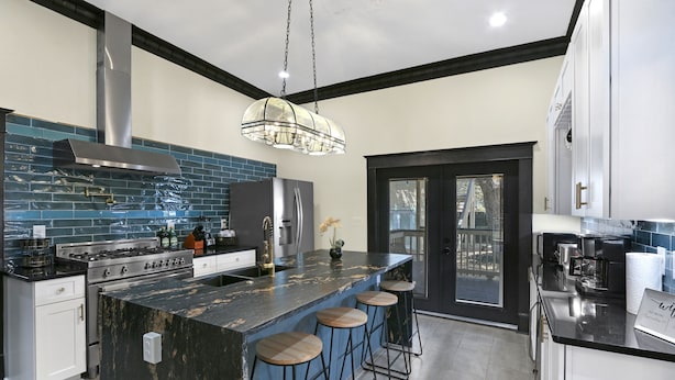 Een moderne keuken met een groot eiland, barkrukken, roestvrijstalen apparatuur en een backsplash van zwarte en blauwe tegels.