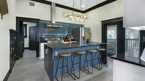 Een moderne keuken met een centraal eiland, barkrukken, een roestvrijstalen koelkast en een blauwe achterwand.