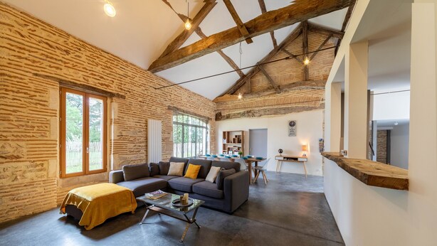 A spacious living area with exposed wooden beams, a stone wall, and a large window.