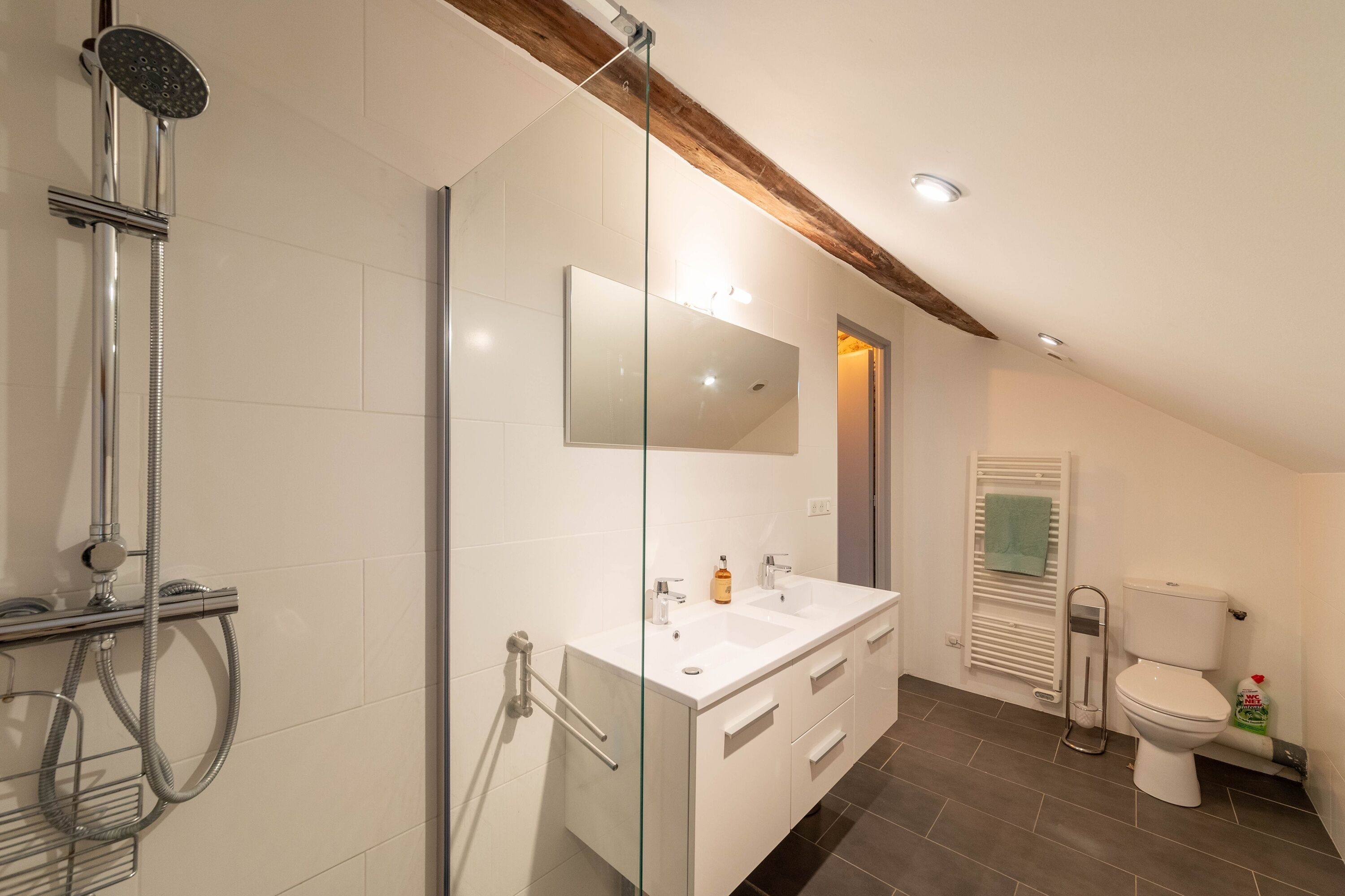 Un baño moderno con cabina de ducha de vidrio, un tocador blanco con espejo y un inodoro.
