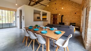 A spacious dining area with a wooden table set for six, white chairs, and a grey sofa in the background.