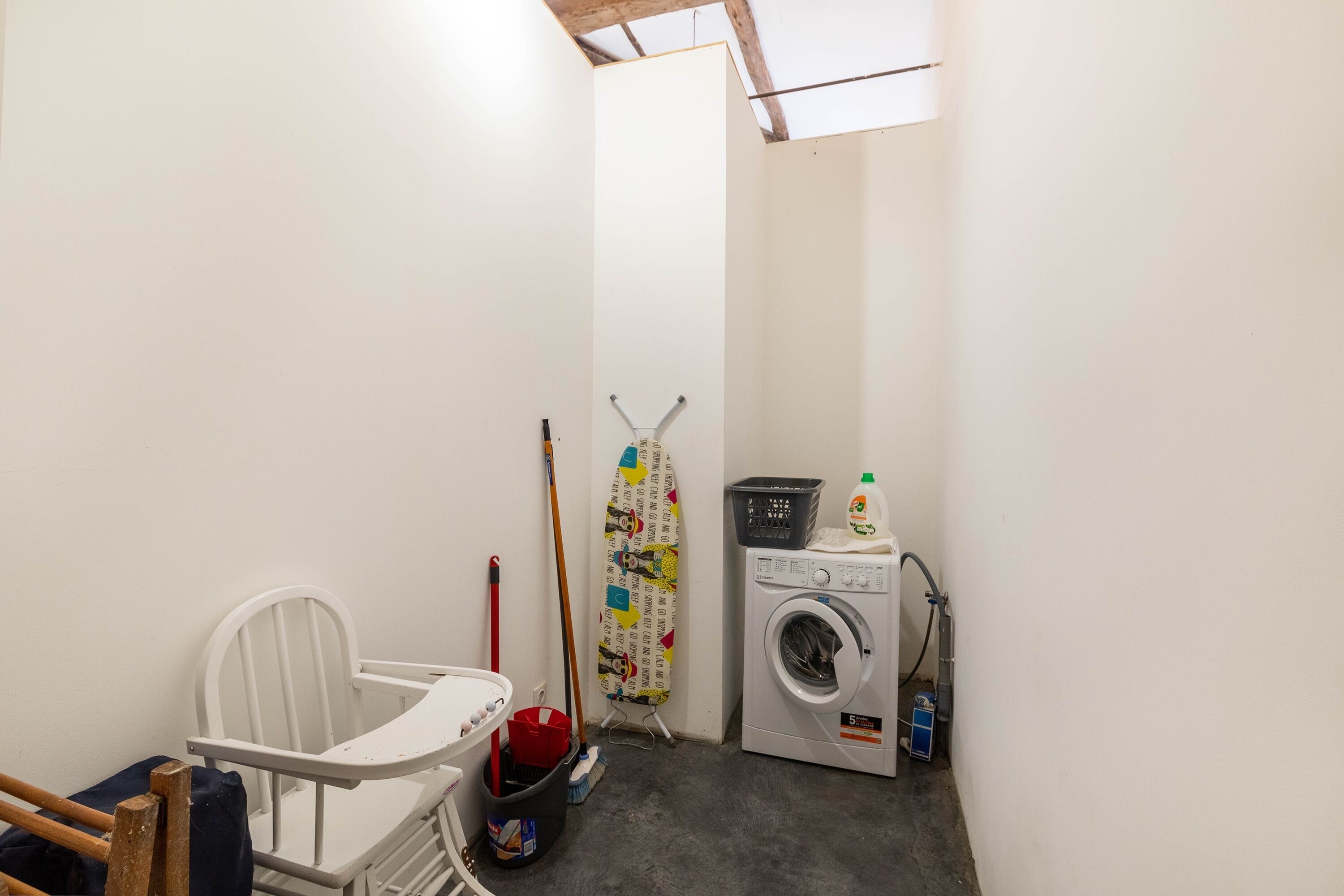 A laundry room with a washing machine, a mop, a broom, and a chair.