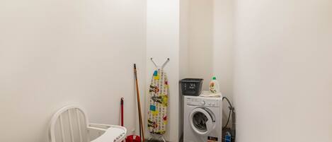 A laundry room with a washing machine, a mop, a broom, and a chair.