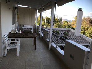 A covered outdoor area with a table and benches, a railing, and a view of greenery and buildings in the background. - Beautiful Spacious apt in Nea Makri (Marathon)