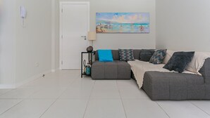 A living room with a grey sofa, a painting of a beach scene, a lamp, and a small table with a basket. - 350m from the Beach | Pool | Barbecue #IA20 (Florianópolis)