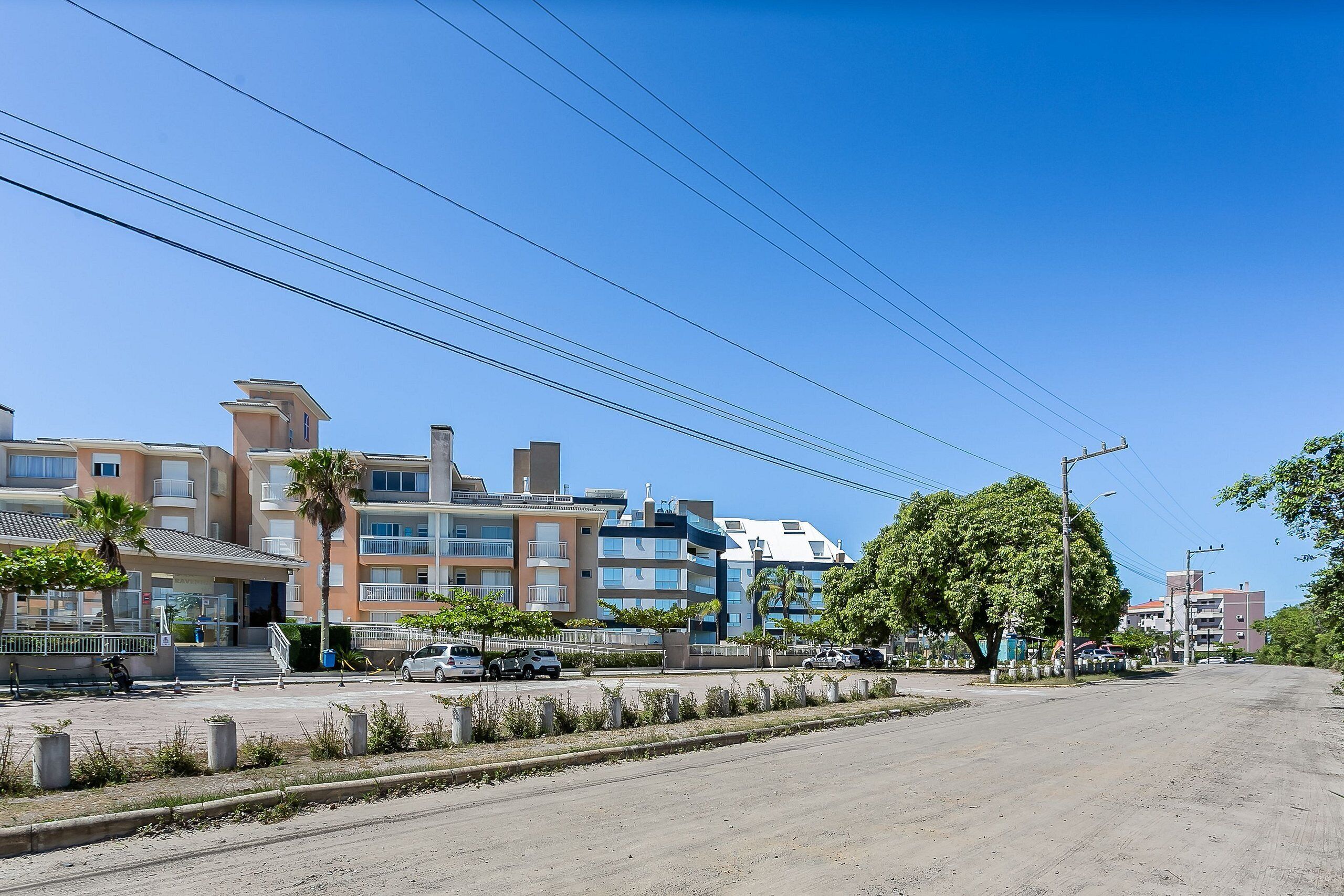 A multi-story residential building with balconies, a parking area, and a clear blue sky.