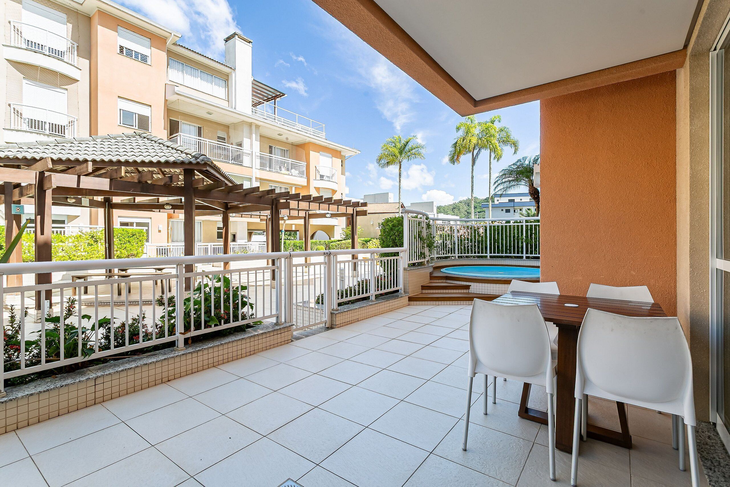 A balcony with a pool, white chairs, and a pergola.