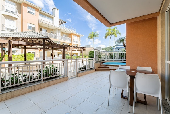 Un balcon avec une piscine, des chaises blanches et une pergola.