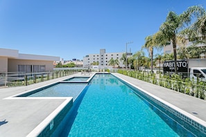 Piscina com água azul cristalina, rodeada por um deck de concreto e palmeiras.