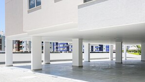 Un espace extérieur couvert et ouvert, doté d’un sol carrelé et de piliers blancs, qui fait probablement partie d’un hôtel ou d’un bâtiment public.