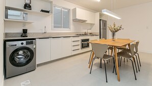 A modern kitchen with a built-in washer, a dining area with a wooden table and chairs, and a large window providing natural light.