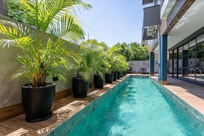 Uma piscina com plantas em vasos de um lado e um edifício com grandes janelas do outro.