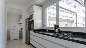 A modern kitchen with a gas stove, built-in oven, and a window overlooking a residential area. - Gastronomy | 120m from the Beach | Pool #CAMP07 (Florianópolis)