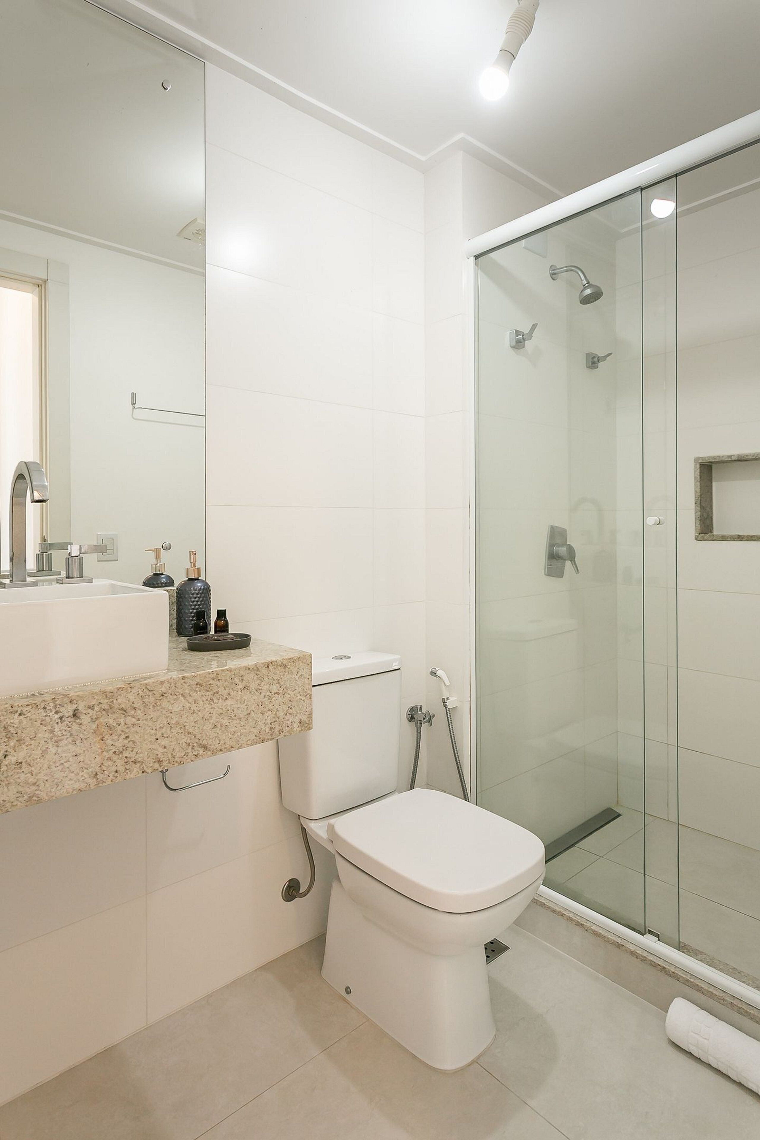 Een moderne badkamer met een douchecabine van glas, een wit toilet en een granieten aanrecht met een wastafel en spiegel.