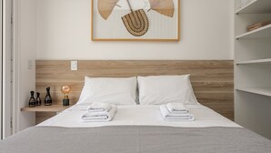 A neatly made bed with white linens and towels, a wooden headboard, and a framed artwork above the bed. - Gastronomy | 120m from the Beach | Pool #CAMP07 (Florianópolis)
