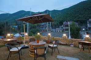 An outdoor seating area with wicker chairs and a round table, surrounded by stone walls and potted plants, overlooking a mountainous landscape. - Moganshan Yishang Inn (Deqing)