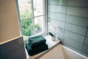 Ein Badezimmer mit Fenster, einer Badewanne und einem Blumentopf.