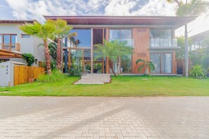 Ein modernes, zweistöckiges Haus mit gepflasterter Auffahrt, großen Fenstern und einem gepflegten Rasen mit Palmen.