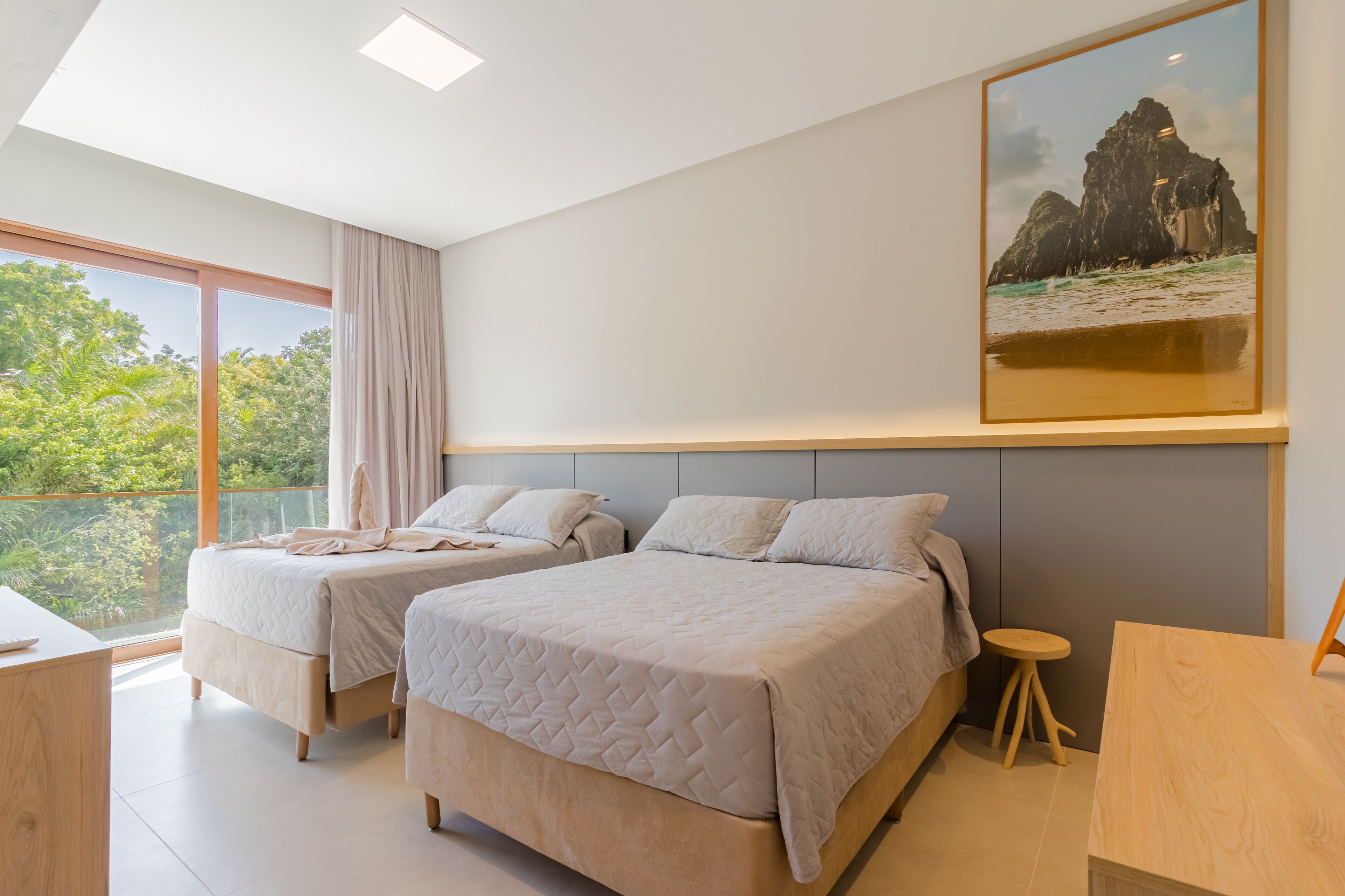 Une chambre moderne avec deux lits, une grande fenêtre et un tableau encadré au mur.