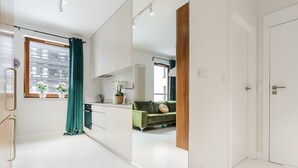 A modern, well-lit room with a large window, a green sofa, and a kitchen area.