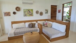 Ein Zimmer mit einer Couchgarnitur aus Holz, einem runden Holzschemel und verschiedenen Wanddekorationen.