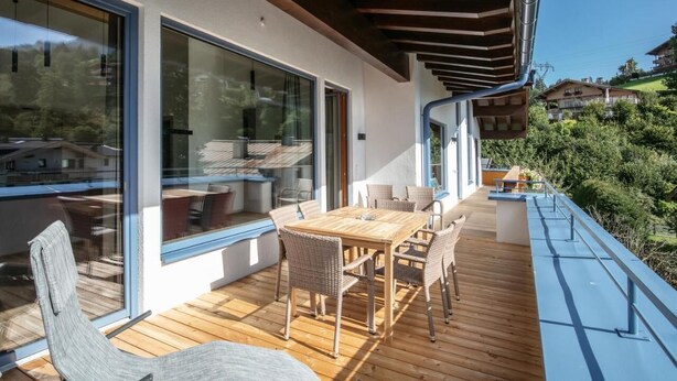 A modern outdoor deck with a wooden table and chairs, large glass doors, and a view of the surrounding landscape. - Appart Hotel Amadeus  (Sankt Johann in Tirol)