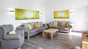 A modern living room with two grey sofas, a wooden coffee table, and abstract paintings on the wall. - Appart Hotel Amadeus  (Sankt Johann in Tirol)