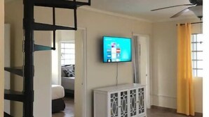 Un'ampia zona giorno con pavimento piastrellato, un tavolo consolle bianco, una televisione a schermo piatto montata a parete e una ventola a soffitto.