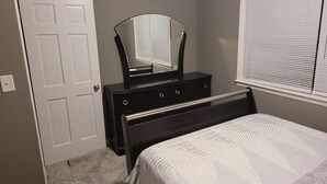 Un dormitorio con cama, cómoda, espejo y ventana con persianas.