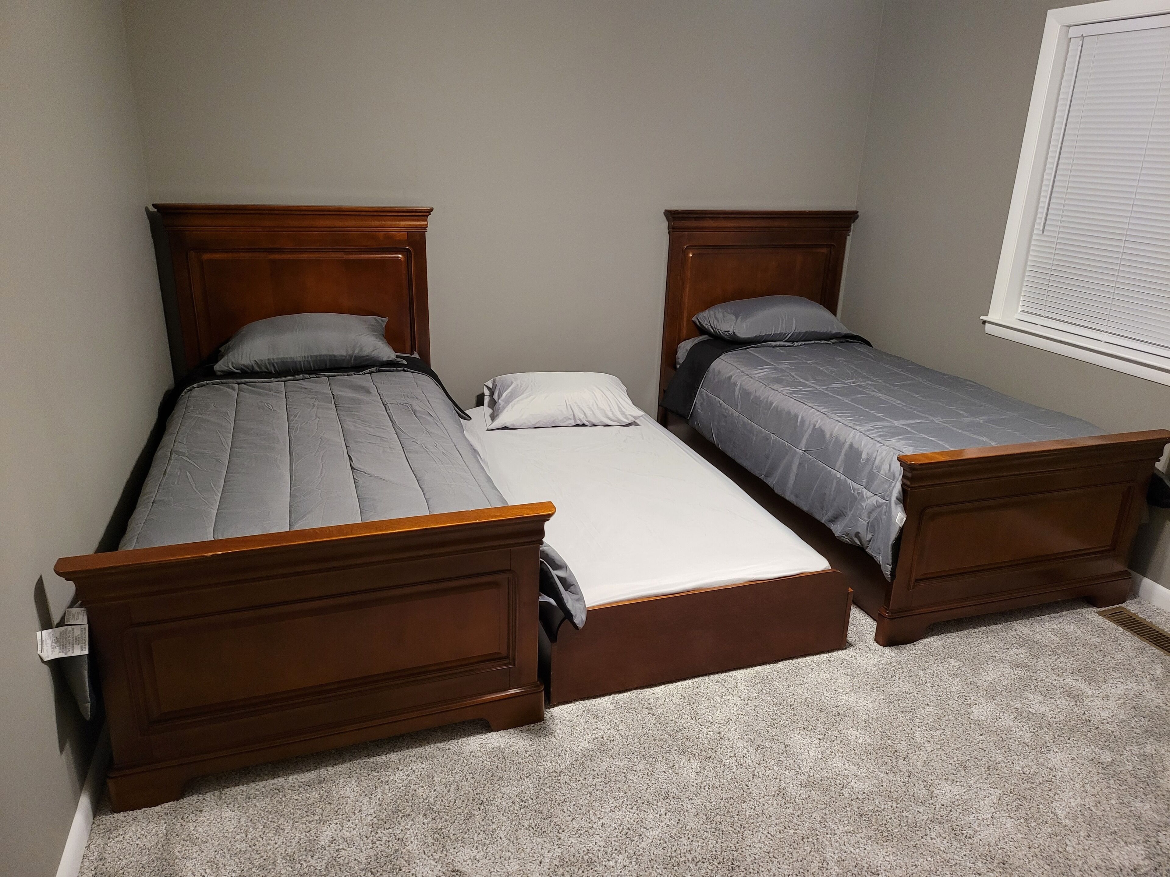 A bedroom with two single beds, a wooden headboard, a white mattress, and a carpeted floor.