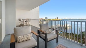 Ein Balkon mit zwei Stühlen und einem Tisch, der auf einen Jachthafen mit Booten und Gebäuden im Hintergrund blickt.