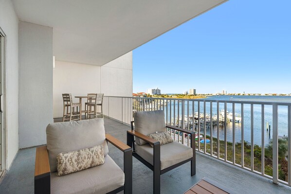 A balcony with two chairs and a table, overlooking a marina with boats and buildings in the distance.